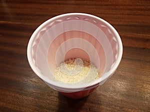 Red plastic cup of rice on brown wood table