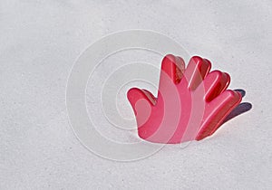 Red plastic hand toy on a white sand beach