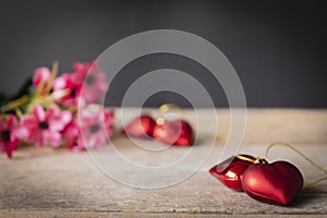 Red plastic hearts placed on a wooden table There is a flower placed on the left back There are red plastic hearts placed backside