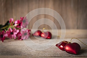 Red plastic hearts placed on a wooden table There is a flower placed on the left back There are red plastic hearts placed backside