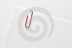 Red plastic paper clip attached to the corner of a blank white paper