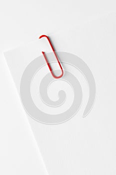 Red plastic paper clip attached to the corner of a blank white paper