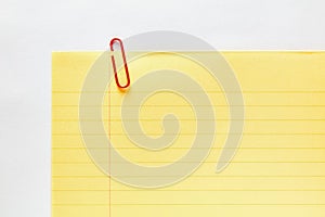 Red plastic paper clip attached to the corner of a blank yellow ruled or lined notebook paper