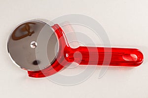 A red plastic pizza cutter with a silver handle