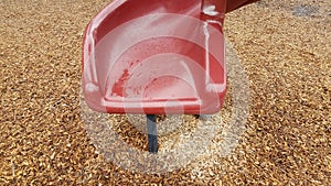 red plastic playground slide with wood chips on ground