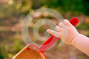 Red plastic scoop scoop in a children`s hand. Play in the sandbox. With a scoop of sand falls. Symbol of childhood and fun