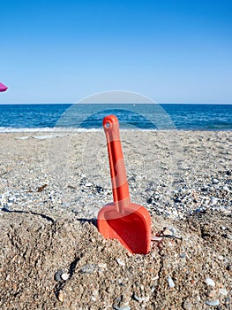 Red plastic shovel for children stuck in the sand on the beach in front of the sea