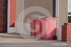 Red plastic wheelie bins in drive way by a house. Recycle industry. Waste containers ready for collection in a residential area