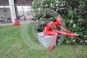 Red plastic womae sculptures. Blooming tree background.