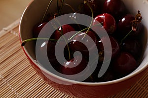 Red plate with dark cherries on the table