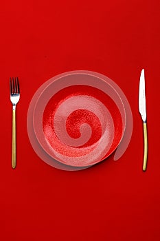 Red plate, knife and fork on a red table. Top view. Copy space