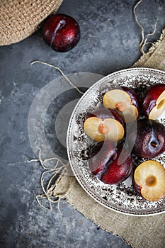 Red plums on a vintage plate on a gray background. Pieces of fresh seasonal fruits.