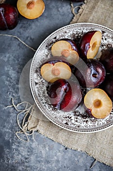 Red plums on a vintage plate on a gray background. Pieces of fresh seasonal fruits.