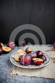 Red plums on a vintage plate on a gray background. Pieces of fresh seasonal fruits.