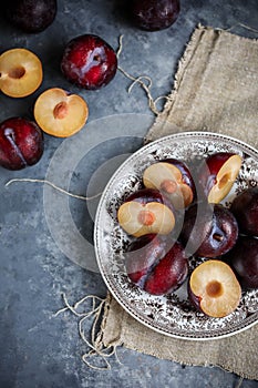 Red plums on a vintage plate on a gray background. Pieces of fresh seasonal fruits.