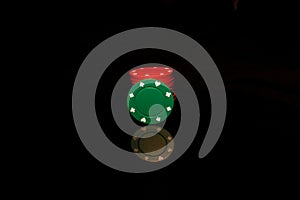 Red pocker chips stack with a green chip in front isolated on black with reflection