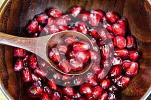 Red pomegranate fruit seeds in a wooden bowl. Pomegranate seeds on a wooden spoon in a bowl
