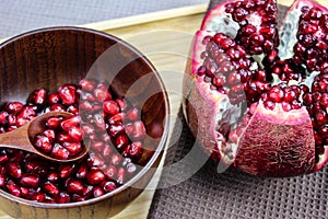Red pomegranate fruit seeds in a wooden bowl. Pomegranate seeds on a wooden spoon in a bowl. Whole ripe pomegranate open on a