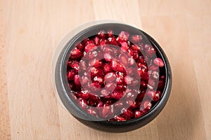 Red pomegranate seeds in black porcelain bowl on wooden background