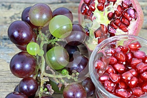 Red Pomegranate seeds and Grapes on the wooden background