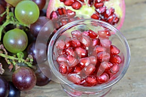 Red Pomegranate seeds and Grapes on the wooden background