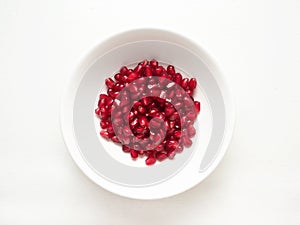 Red pomegranate seeds in a white plate from top view