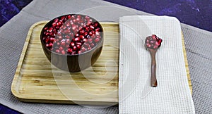 Red pomegranate seeds in a wooden bowl with a wooden spoon with the seeds next to the napkin. Red pomegranate seeds served on a