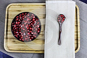 Red pomegranate seeds in a wooden bowl with a wooden spoon with the seeds next to the napkin. Red pomegranate seeds served on a