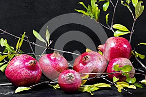 Red pomegranates with green leaves on wooden old cutting board, side view, dark background