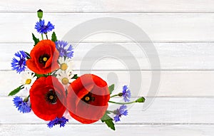 Red poppies, cornflowers and chamomile on background of white painted wooden planks with space for text. Top view, flat lay