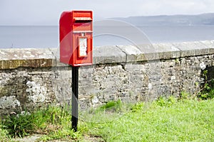 Red post box in Scottish rural location brightly lit under dark sky