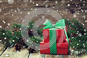 Red present box with bow ribbon decoration of fir tree and conifer cone with magic snow effect on wooden rustic board