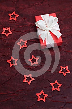 Red present with a white bow on a red shimmering cloth, surrounded by red cut out stars.