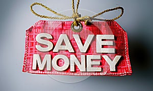 Red promotional tag with golden string stating SAVE MONEY in bold white letters, symbolizing financial savings and budgeting