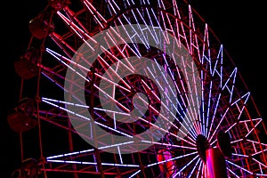 Red and purple light fluorescent on structure of ferris wheel with dark night background