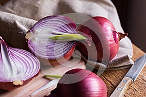 Red or purple onion cut in half, green germs, wood breadboard, linen towel, knife, kitchen table by window