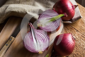 Red or purple onion cut in half, wood breadboard, linen towel, knife, kitchen table by window