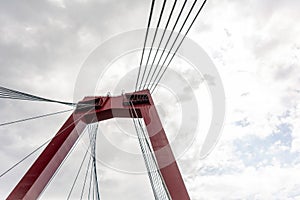 Red pylon and cables of Willemsbrug bridge against cloudy sky