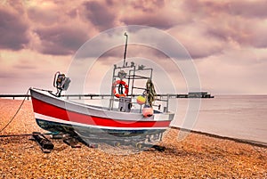 Red quaint, traditional fishing boat moored on the pebble shingle beach in Deal, Kent, UK with the pier in the background