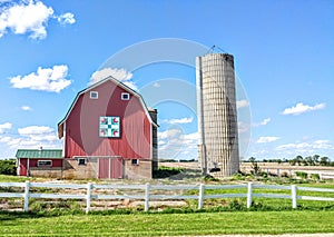 Red Quilt Barn with a Silo and a White Fence