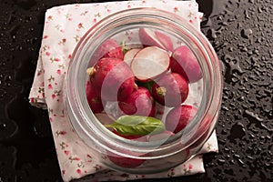 Red radish with basil leaf in glass jar on black water drop background.