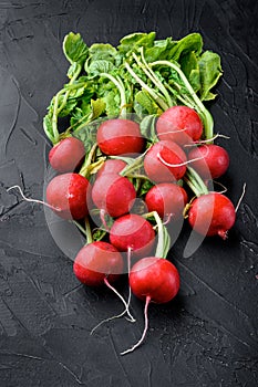 Red radish bunch with green leaves, on black stone background