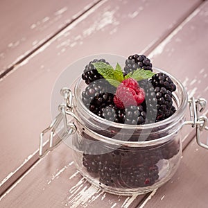 Red raspberries and blackberries in a glass jar with a leaf of mint, 1x1 size