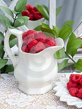 Red raspberries  and green leaves on white laced tablecloth.