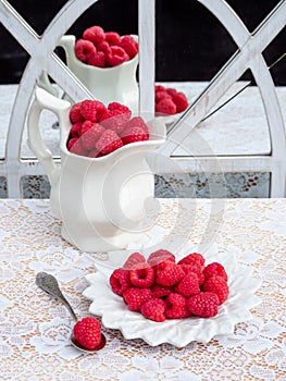 Red raspberries in white plate and pitcher reflecting in old mirror.