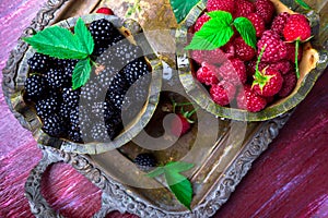 Red raspberry and blackberry with leaf in a basket on vintage metal tray. Top view.