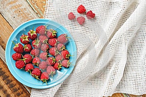 Red raspberry in blue dish and in front of white fabric on old vi