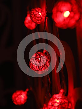 Red Rattan ball garland on patterned wall. Christmas led lights on dark background. Blurred glowing light bulb garland. Closeup