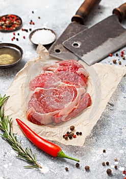 Red raw beef rib eye steak fillet with steel hatchets on light background with salt and pepper