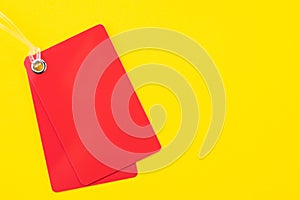 Red rectangle blank plastic red price tag label with transparent string on vivid yellow background with copy space, using for